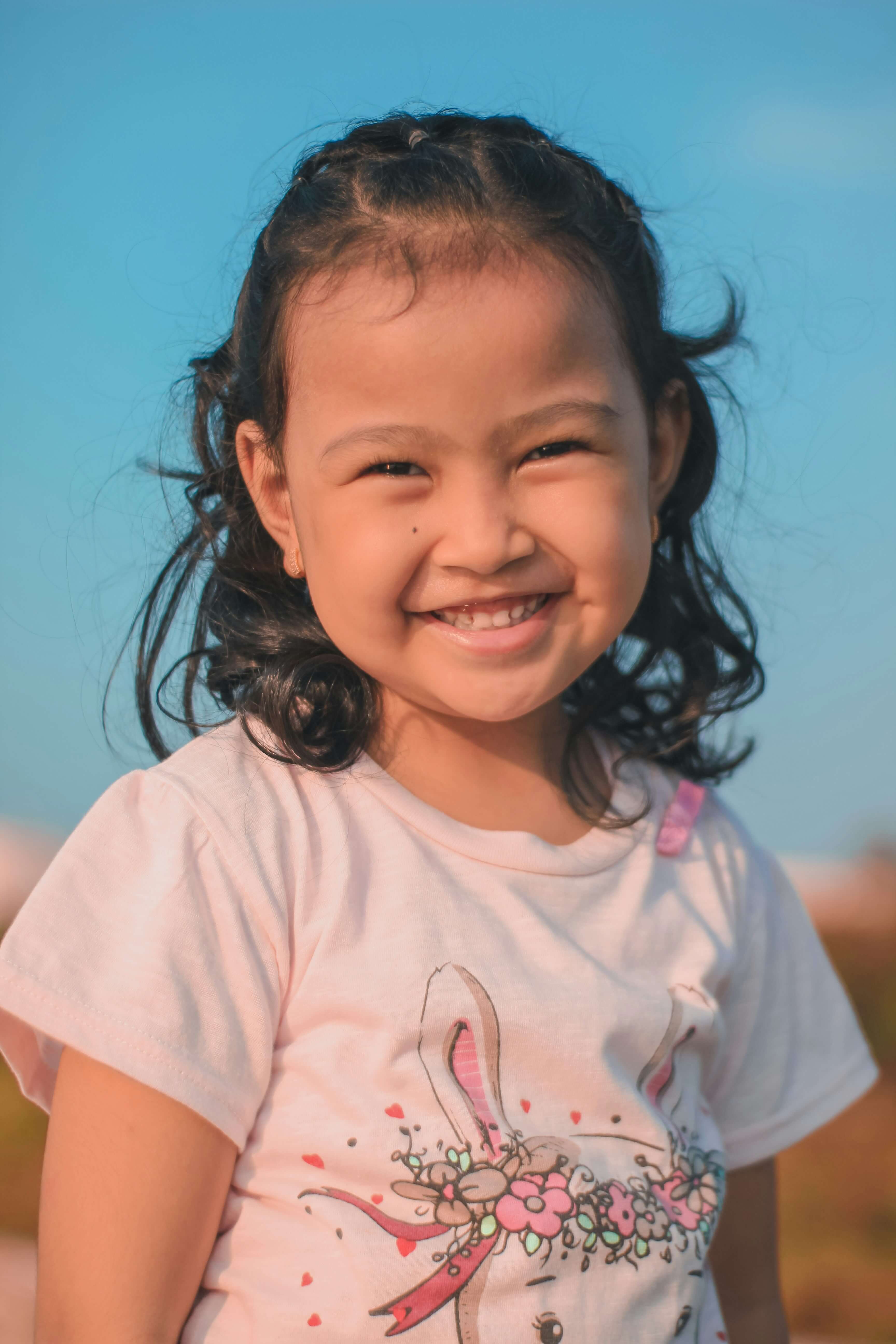 This is a photograph of an Asian girl, approximately four to five years old. She is standing outside at a beach, a communi...